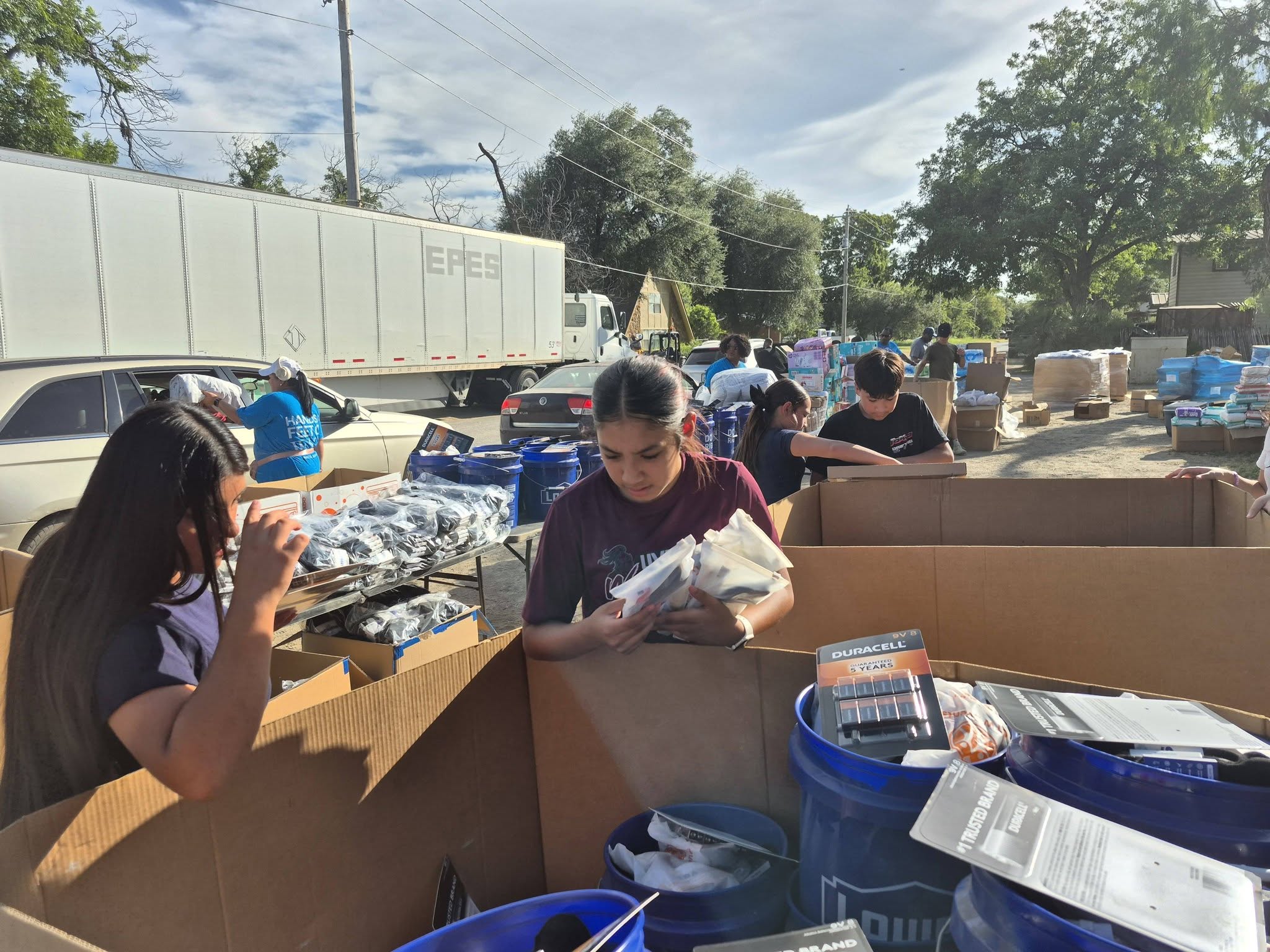 Two young volunteers sorting batteries and hygiene supplies into cardboard boxes at the distribution site