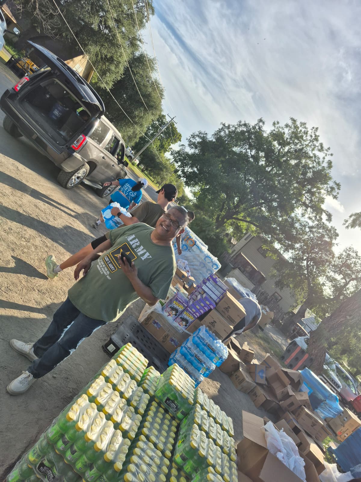 A smiling volunteer in a green Army shirt standing next to pallets of water and snacks ready for distribution
